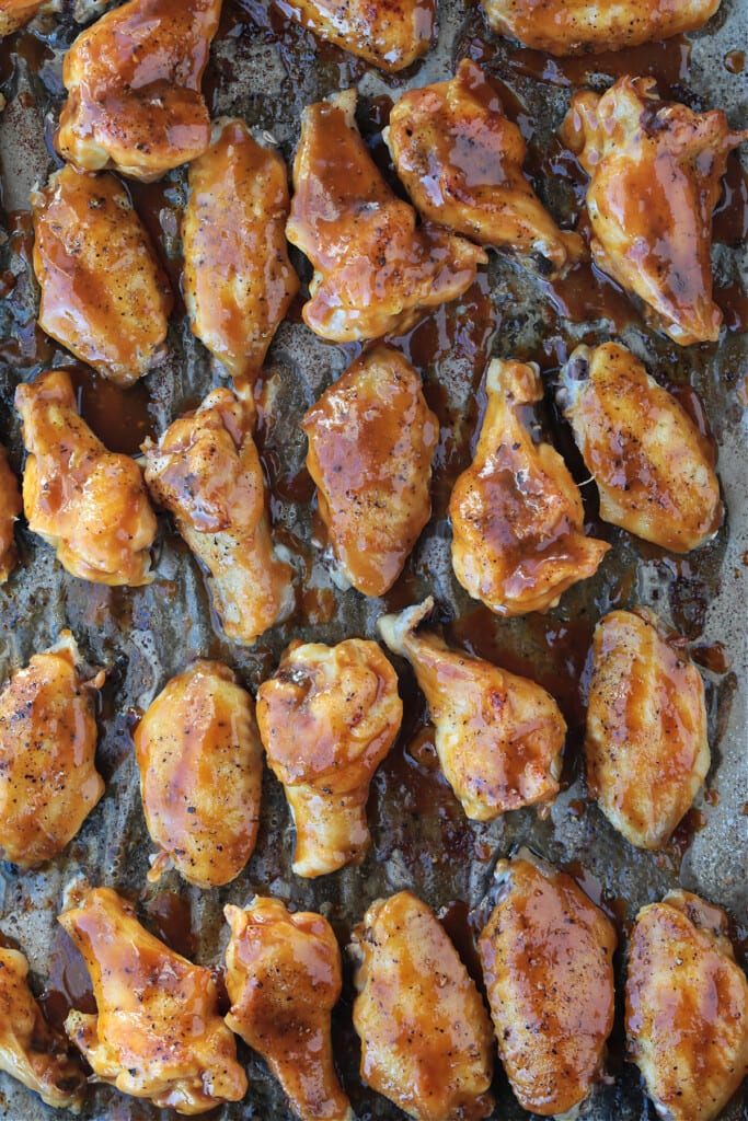 These Asian Chicken Wings are oven baked until tender, with a sticky, sweet addicting sauce. Perfect for appetizers or a fun dinner! chicken wings with sauce on a baking sheet