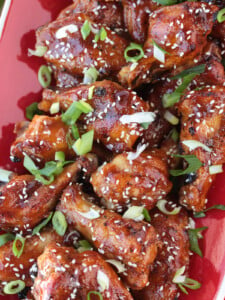 Asian chicken wings on a red platter with sesame seeds and scallions