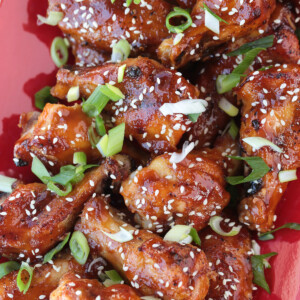 Asian chicken wings on a red platter with sesame seeds and scallions