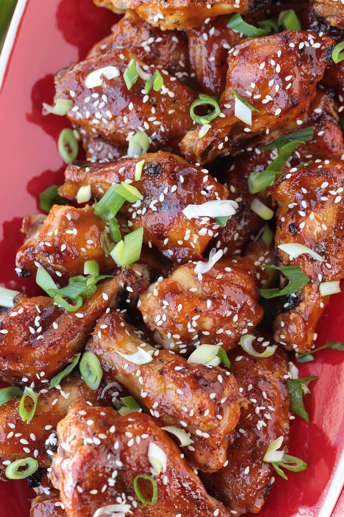 Asian chicken wings on a red platter with sesame seeds and scallions