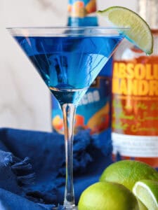 blue martini with lime garnish and limes on the side