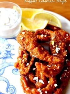 A pile of Buffalo Calamari Strips on a plate with lemons and blue cheese