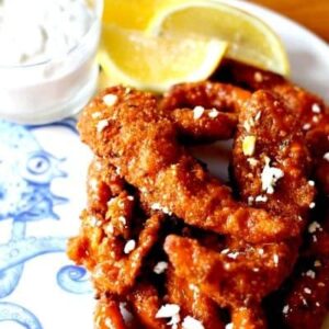 A pile of Buffalo Calamari Strips on a plate with lemons and blue cheese