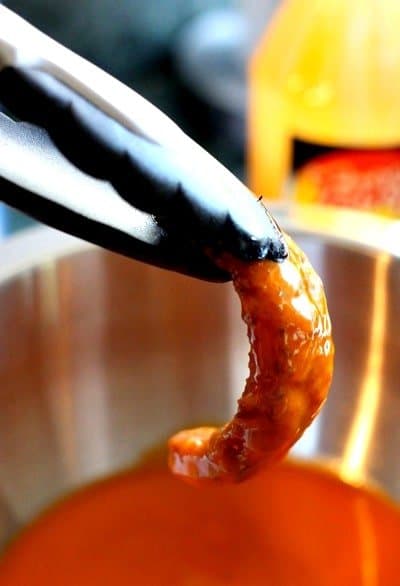 Tongs holding a calamari strip dunked in buffalo sauce