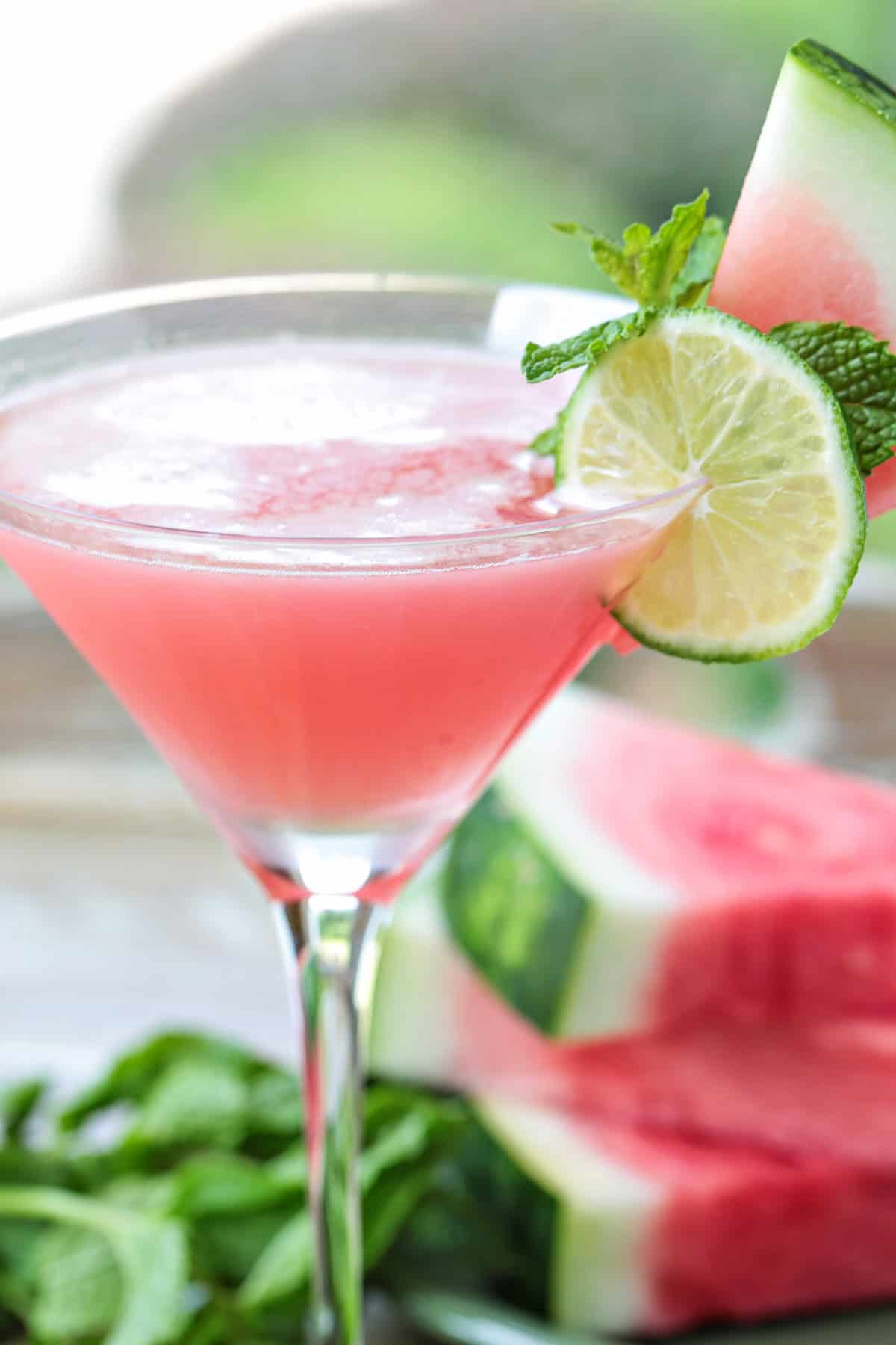 This Watermelon Cosmopolitan is the ultimate summer drink! So light and refreshing, made with fresh watermelon juice and a hint of lime! watermelon cosmopolitan with sliced watermelon in background
