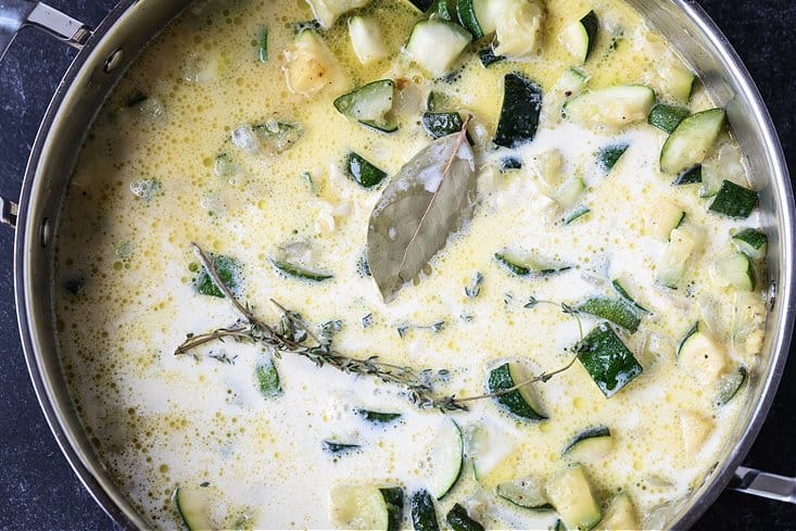 Cream and chicken broth in a skillet with fresh herbs, zucchini and onions