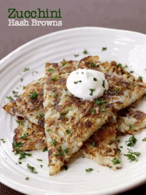zucchini hash browns stacked on a plate with sour cream