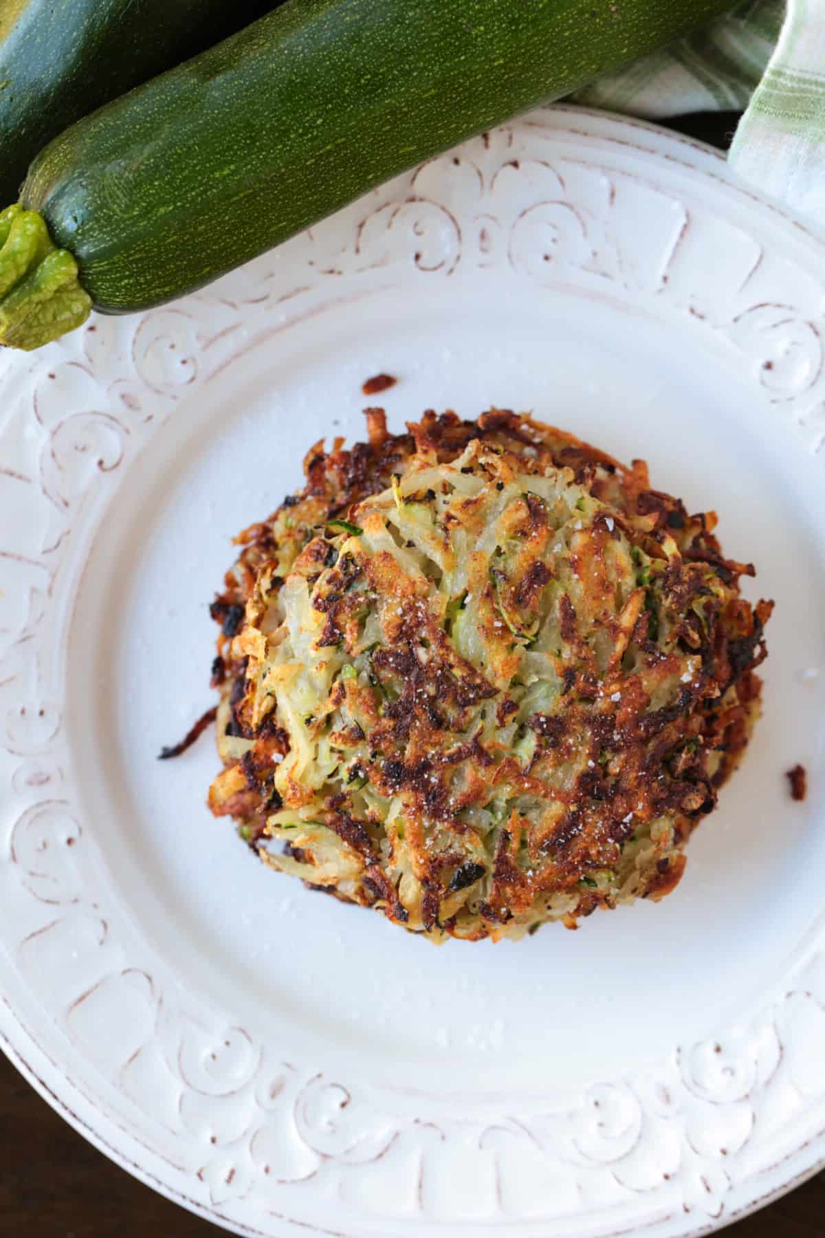 stacked zucchini hash browns on a plate with zucchini on the side