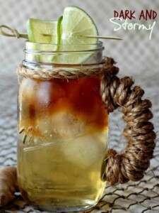 A Dark and Stormy cocktail in a mason jar cup with limes
