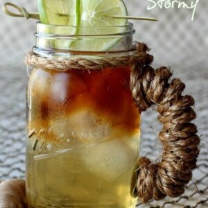 A Dark and Stormy cocktail in a mason jar cup with limes