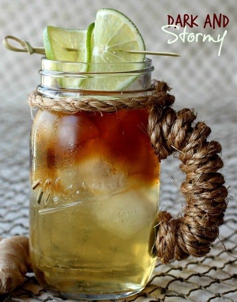 A Dark and Stormy cocktail in a mason jar cup with limes