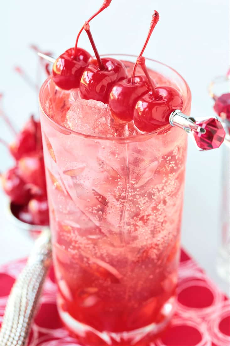A cocktail in a highball glass garnished with cherries