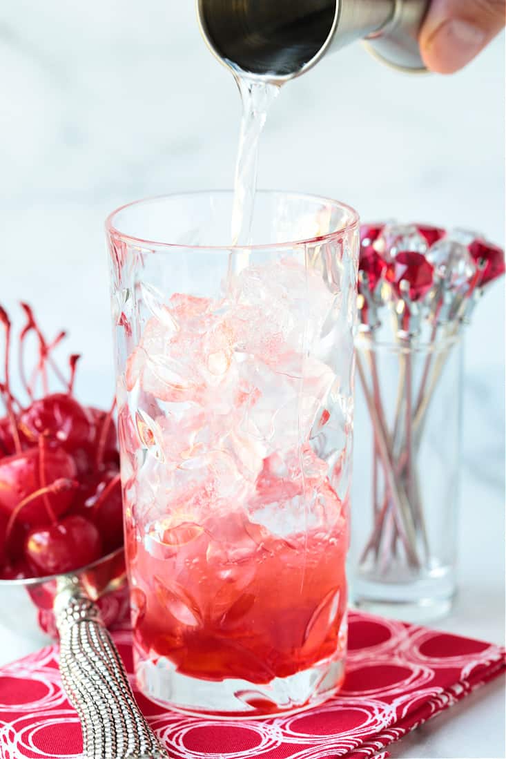 Vodka being poured into a high ball glass with grenadine
