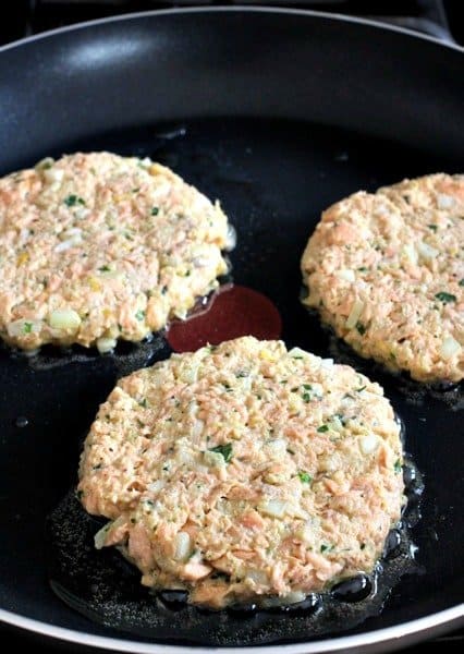 Three raw salmon burgers being cooked in a pan