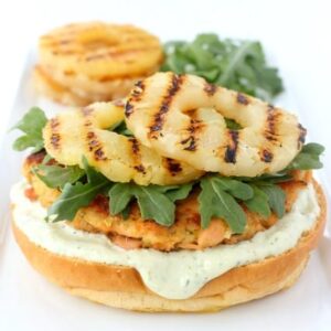 A Salmon Burger with pineapple on top and the top bun missing
