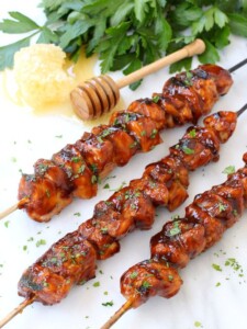 Honey BBQ Chicken Kabobs on a marble board with a honey stick