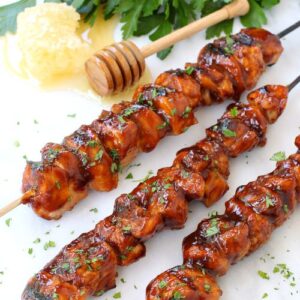 Honey BBQ Chicken Kabobs on a marble board with a honey stick