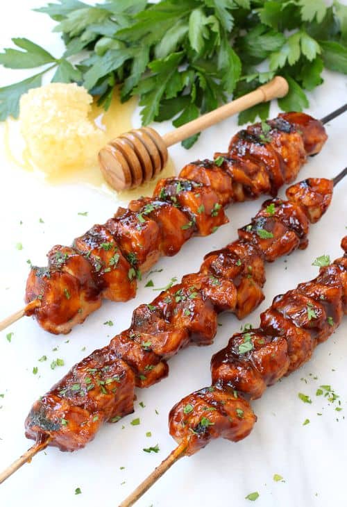 Glazed kabobs on a white surface with honey and herbs