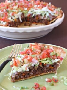 A slice of taco pie loaded with lettuce, tomatoes, meat and cheese on a green plate