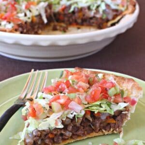 A slice of taco pie loaded with lettuce, tomatoes, meat and cheese on a green plate