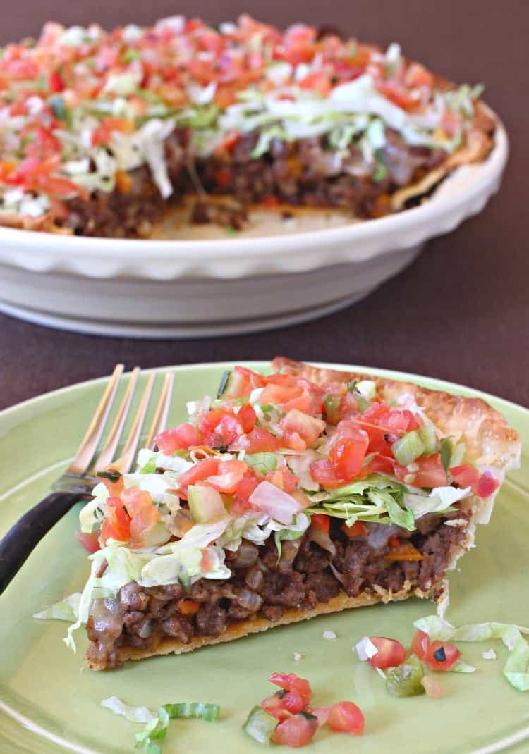 A slice of taco pie loaded with lettuce, tomatoes, meat and cheese on a green plate