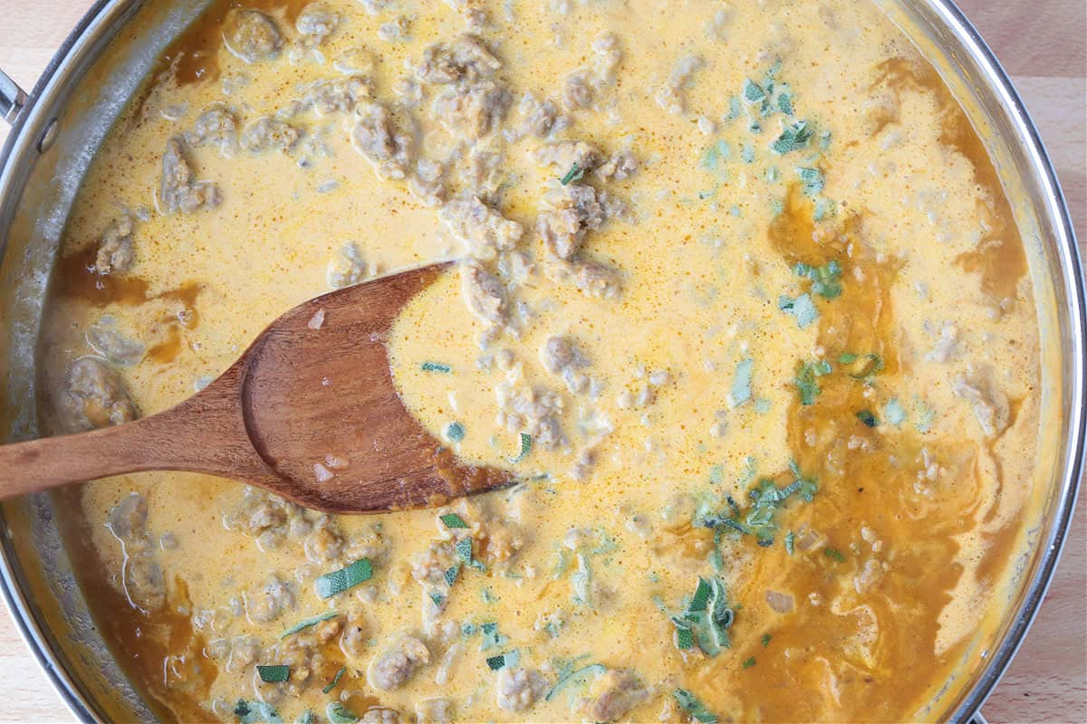 cream, sausage and pumpkin in a skillet with wooden spoon
