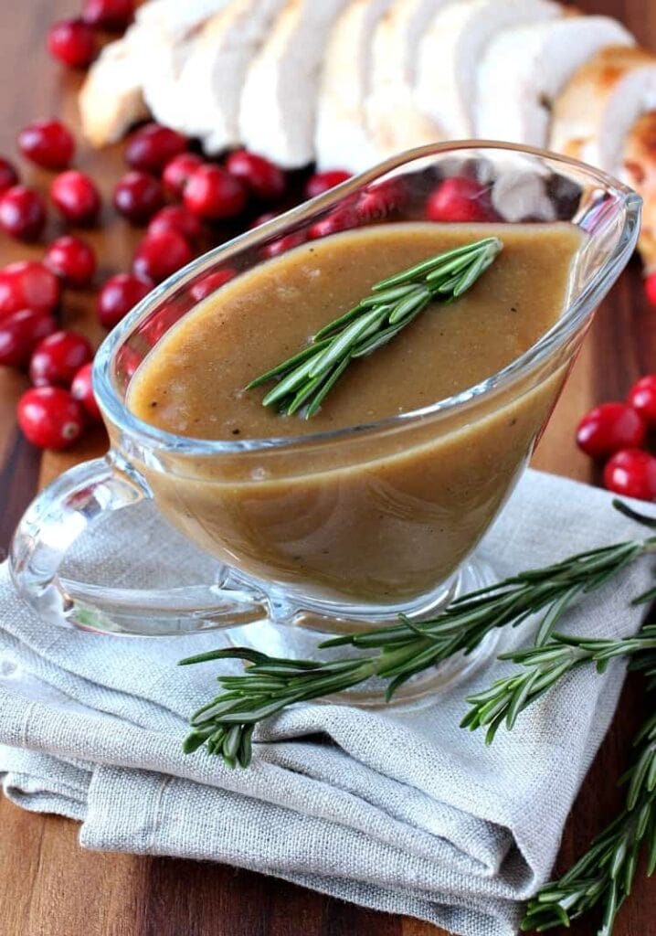 Cranberry Whiskey Gravy in a gravy boat with rosemary and fresh cranberries