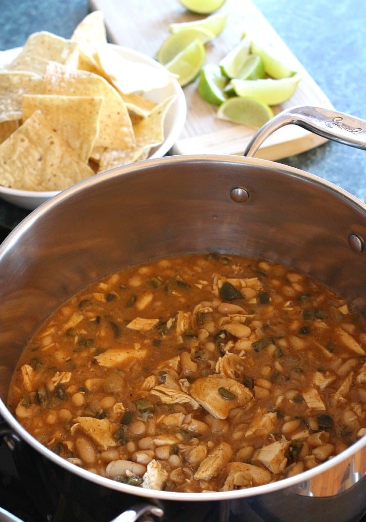 A pot of white bean turkey chili, with a bowl of tortilla chips and a cutting board of lime wedges in the background