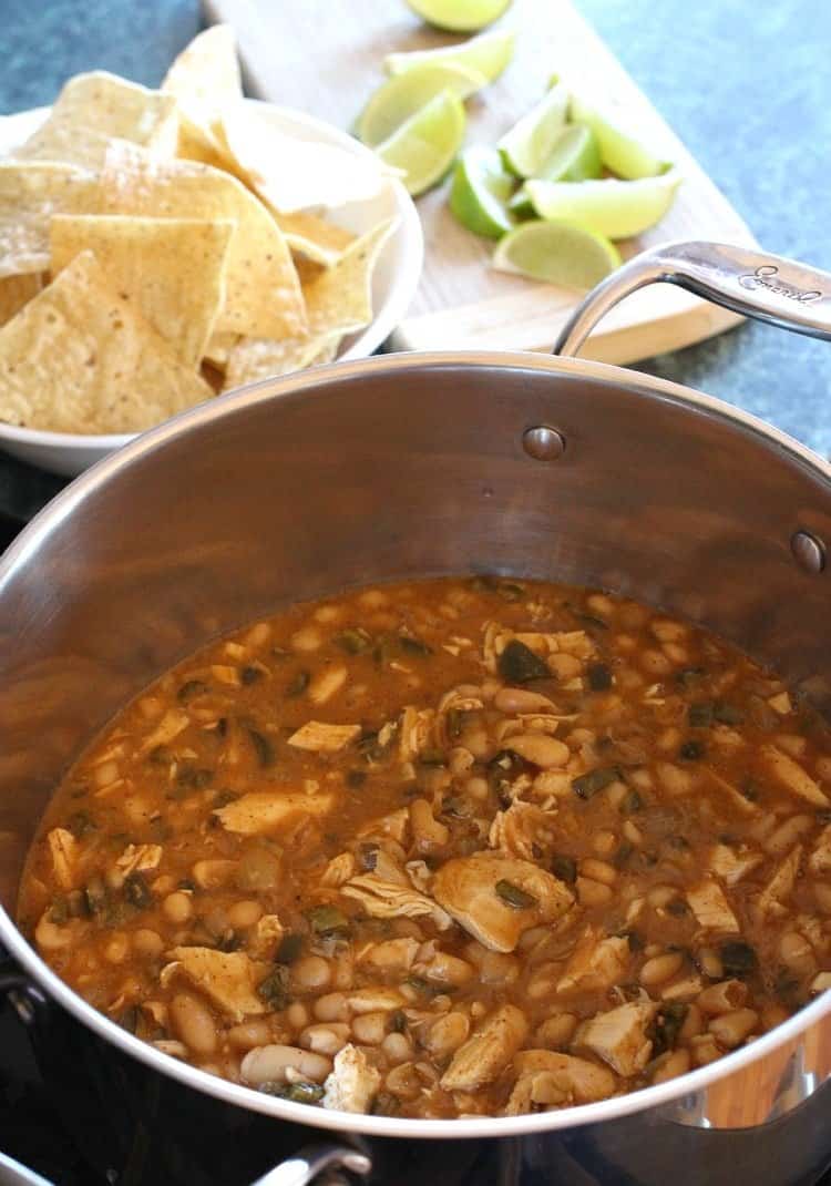 This white bean turkey chili recipe is the perfect way to use leftover Thanksgiving turkey, as it's hearty, spicy, and easy to make. A pot of white bean turkey chili, with a bowl of tortilla chips and a cutting board of lime wedges in the background