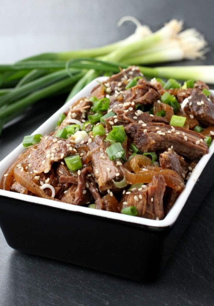 shredded beef in a black bowl with green onions and sesame seeds on top