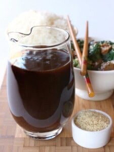 A big glass pitcher filled with homemade Stir Fry Sauce next to a bowl of sesame seeds