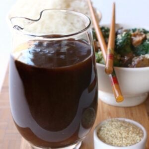A big glass pitcher filled with homemade Stir Fry Sauce next to a bowl of sesame seeds