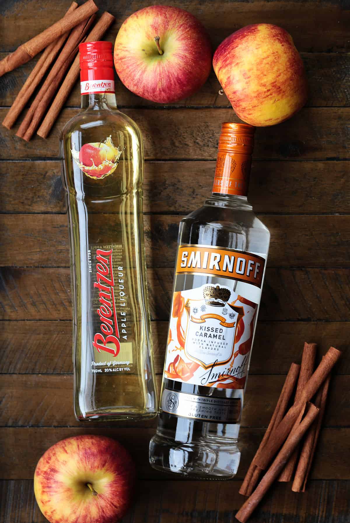 apple liquor and caramel vodka on a wood board with apples and cinnamon sticks