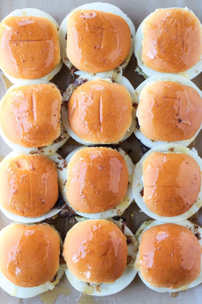 Our French Dip Sliders have a secret sauce that sets them apart from the rest. Beefy, cheesy comfort food perfect for parties and game days! sliders on a baking sheet brushed with butter