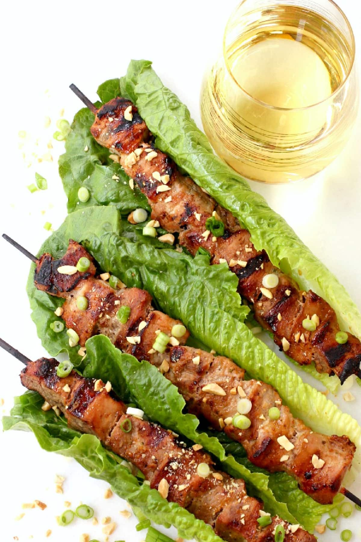 Thai Pork Kabobs have the most delicious sweet and nutty flavor! Wrap in lettuce for easy removal from the skewers and serve with rice! pork kabobs in lettuce leaves with wine on the side