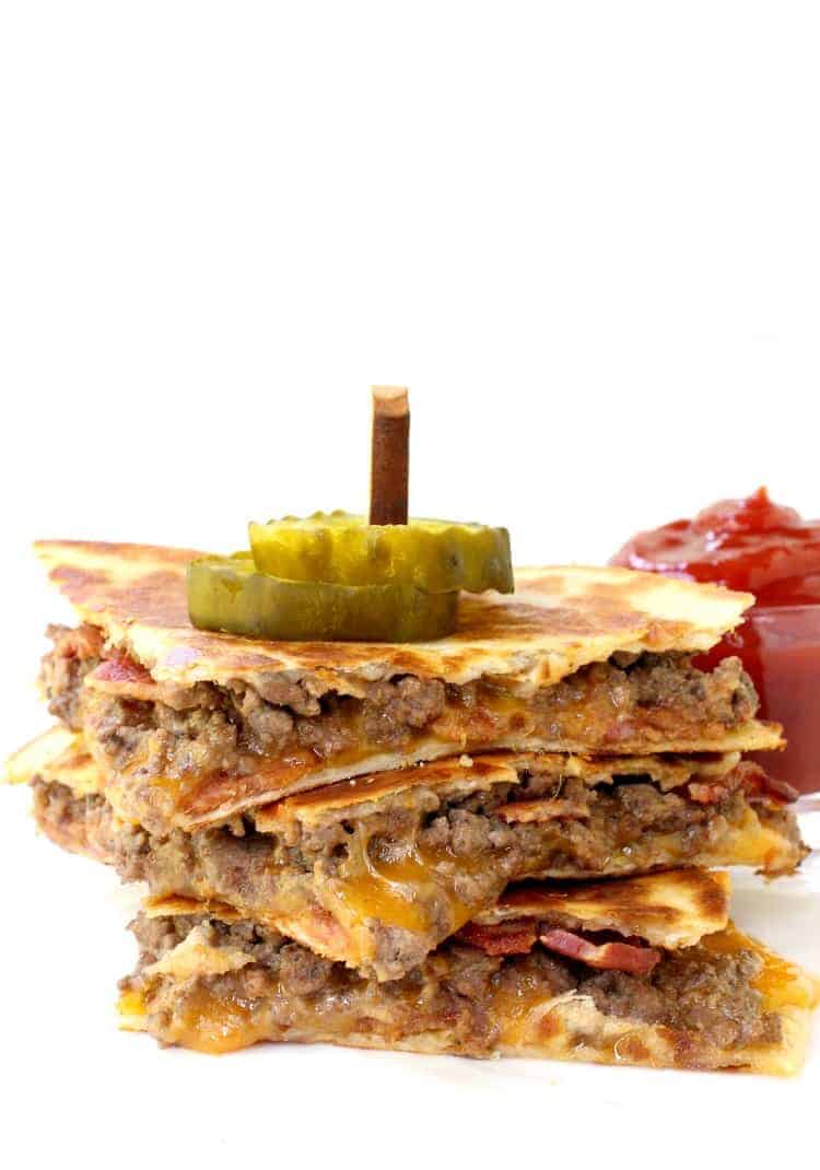 Bacon Cheeseburger Quesadillas stacked on a white plate with pickles