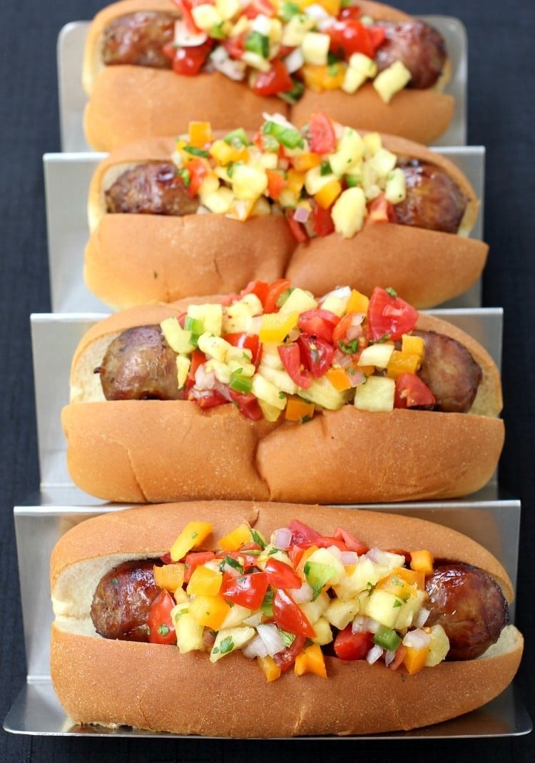 Four bratwurst sausages piled with Pineapple Tequila Salsa on a metal tray.