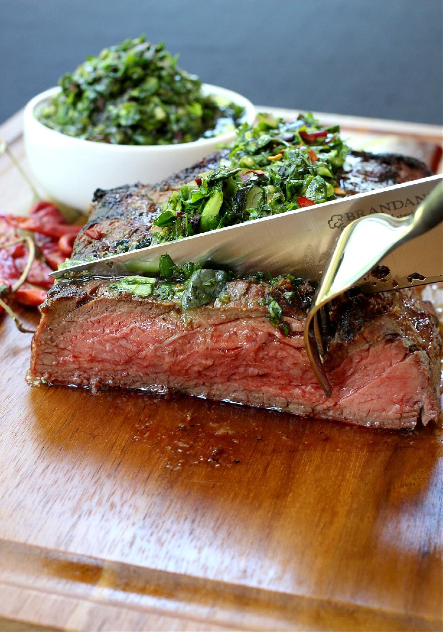 slicing steak with chimichurri sauce on top