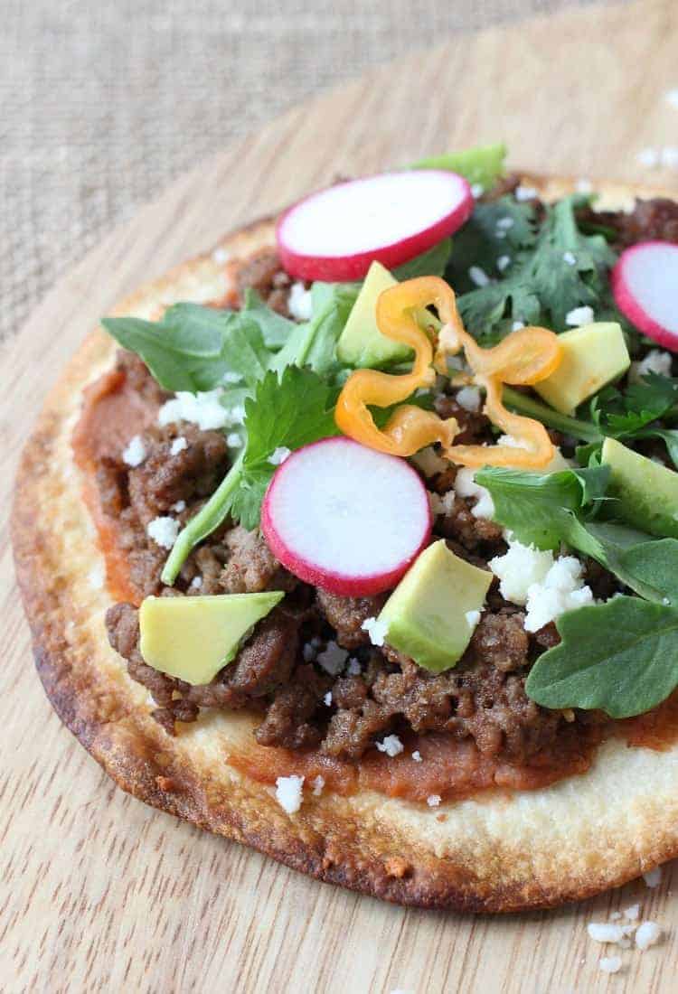 This Spicy Beef Tostada is like a flavor explosion! Crispy tortillas topped with ground beef, refried beans and a fresh crunch from veggies! spicy-mexican-pizzas-close