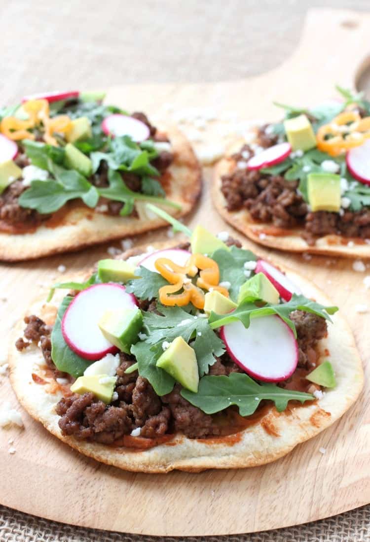This Spicy Beef Tostada is like a flavor explosion! Crispy tortillas topped with ground beef, refried beans and a fresh crunch from veggies! spicy-mexican-pizzas-feature