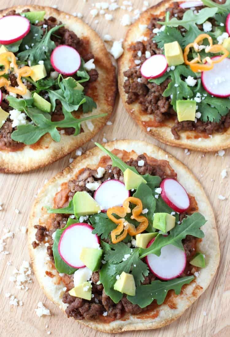 This Spicy Beef Tostada is like a flavor explosion! Crispy tortillas topped with ground beef, refried beans and a fresh crunch from veggies! spicy-mexican-pizzas-top