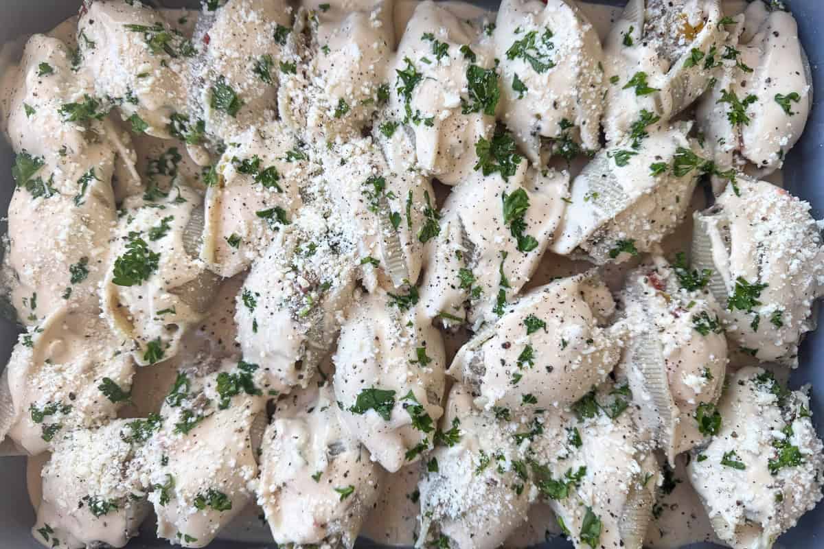 uncooked stuffed shells in baking dish with sauce on top