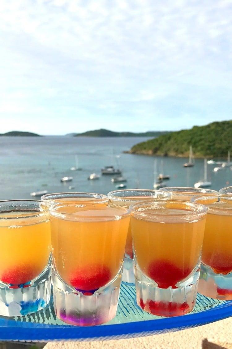 A tray full of pineapple upside down shots on the beach, with water and boats in the background