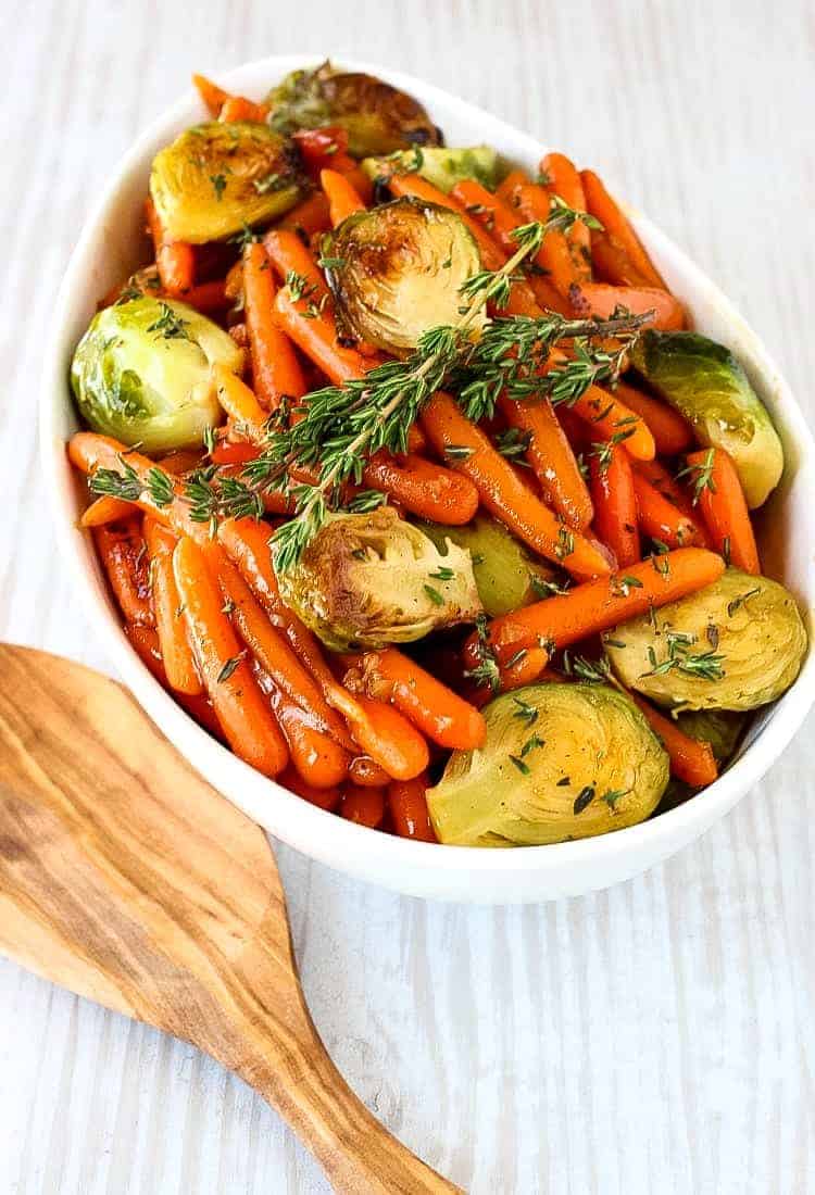 brussels sprouts and carrots in a white bowl with a wooden spoon