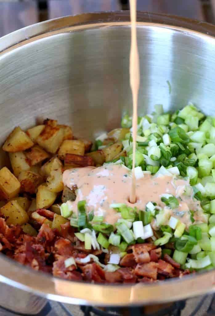 Oven Roasted Barbecue Potato Salad in a silver bowl with ingredients and dressing pouring in