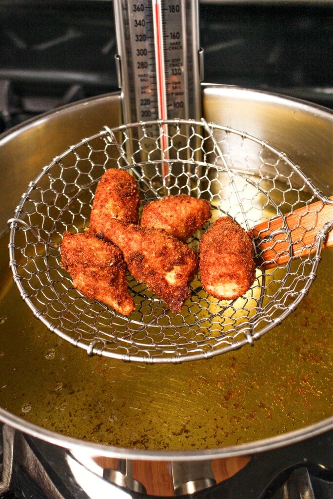 These Fried artichoke hearts are a crispy and addicting appetizer! Make our easy roasted garlic aioli to serve alongside for dipping! fried artichoke hearts coming out of oil