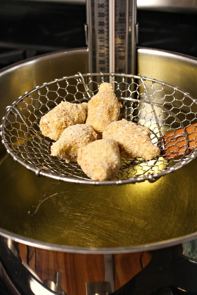 breaded artichoke hearts going into oil for frying