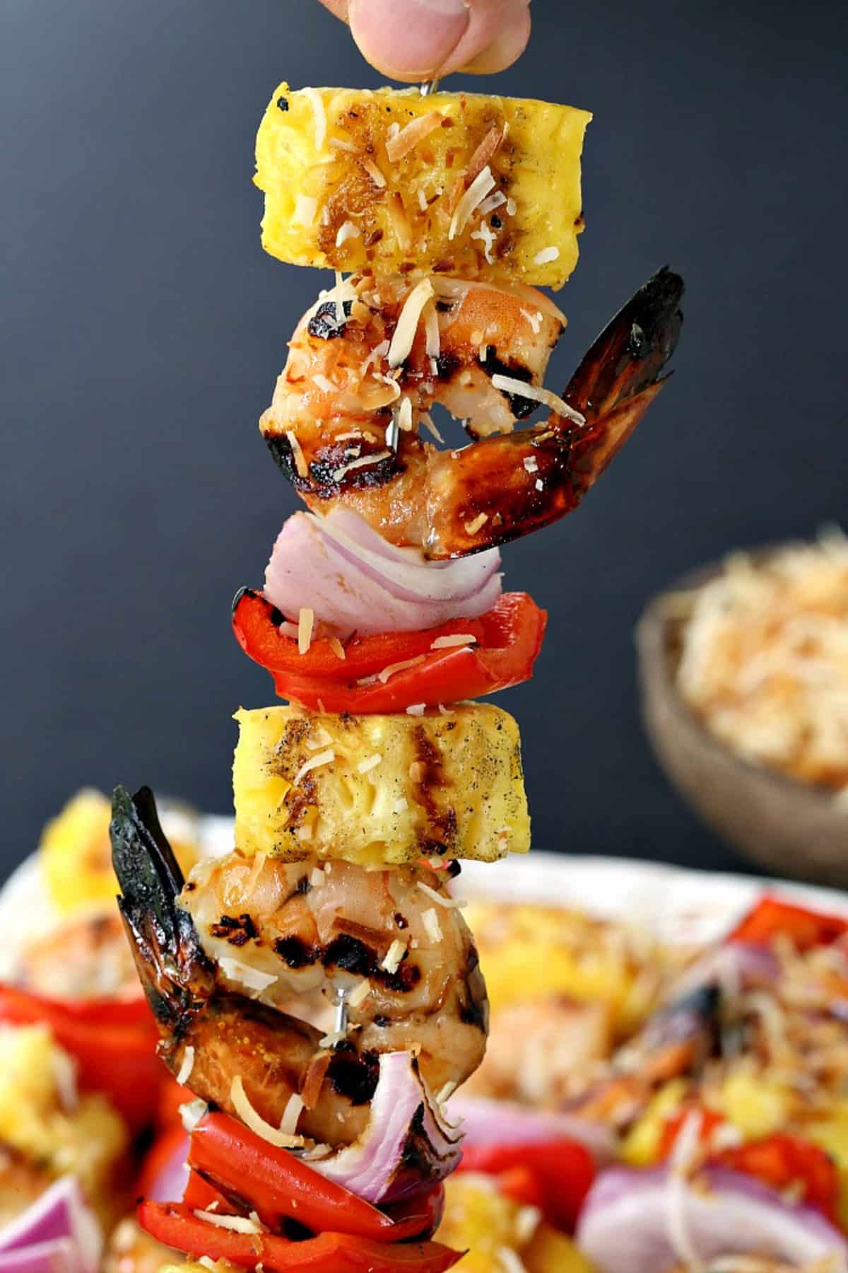Piña Colada Shrimp Kabobs are the ultimate summer dinner! Juicy shrimp with a real piña colada flavor grilled with pineapple and vegetables. holding up one pineapple shrimp kabob