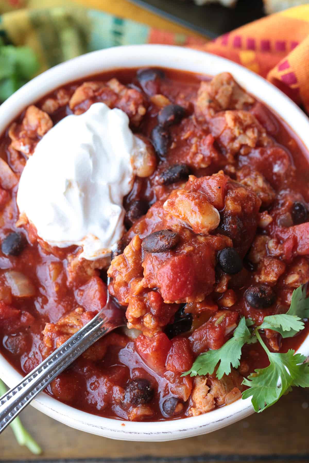 This Chicken Sausage Chili is super hearty and packed with flavor! We like a combo of sweet and spicy sausage, lots of beans and bold spices. chili in a bowl with sour cream and spoon