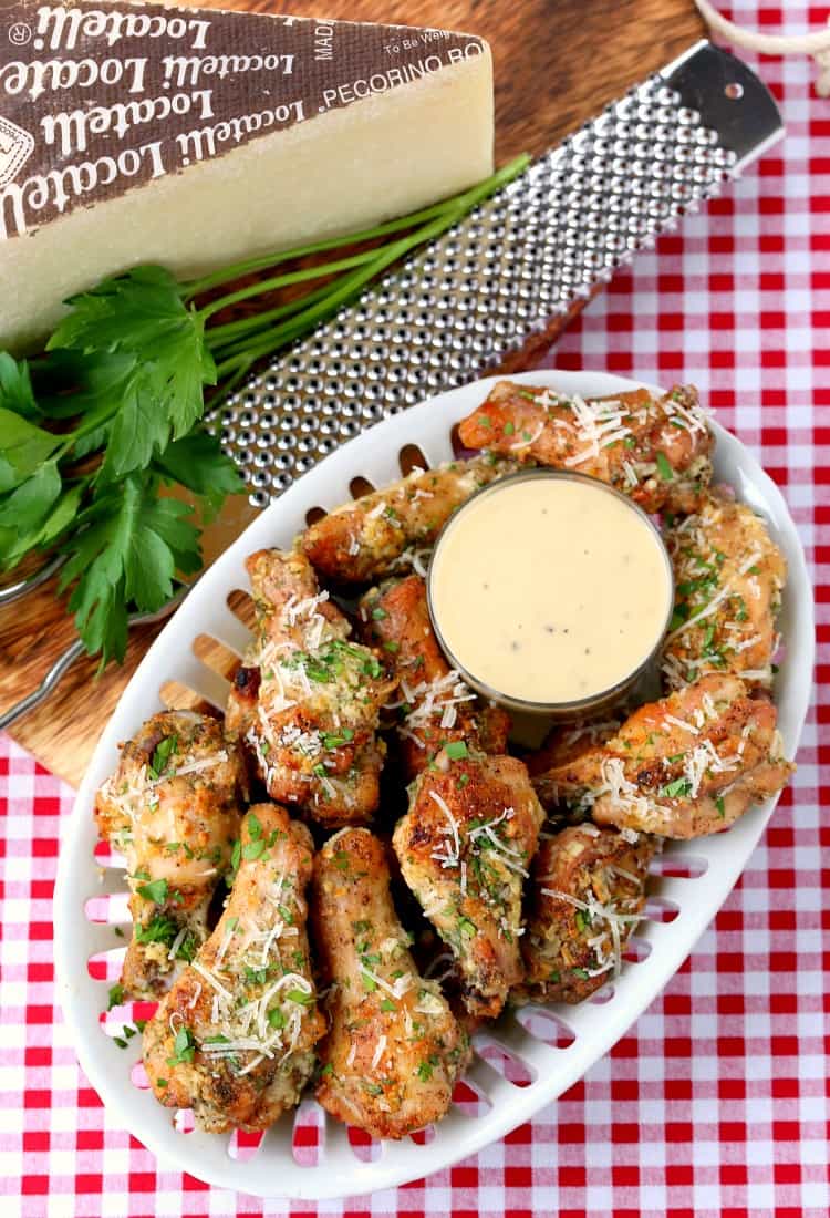 A bird's eye view of a plate of Baked Garlic Parmesan Chicken Wings with a cup of caesar dressing in the middle.